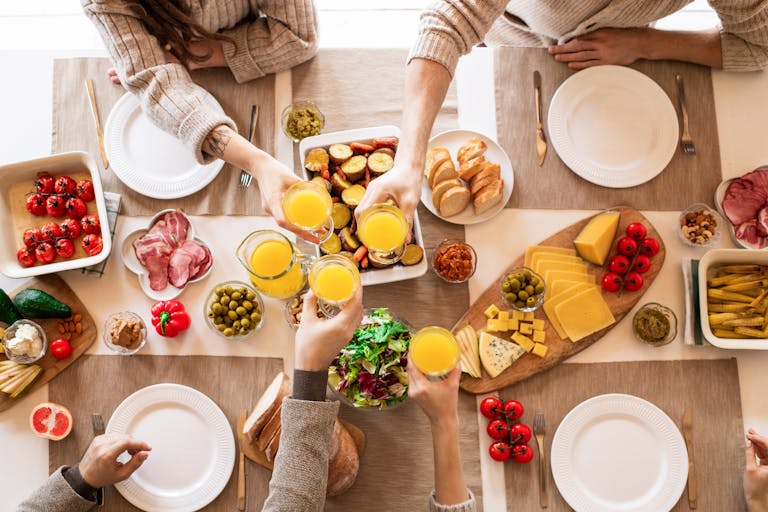 Top view of a family toasting at a lunch table with cheese, olives, and fresh salads.